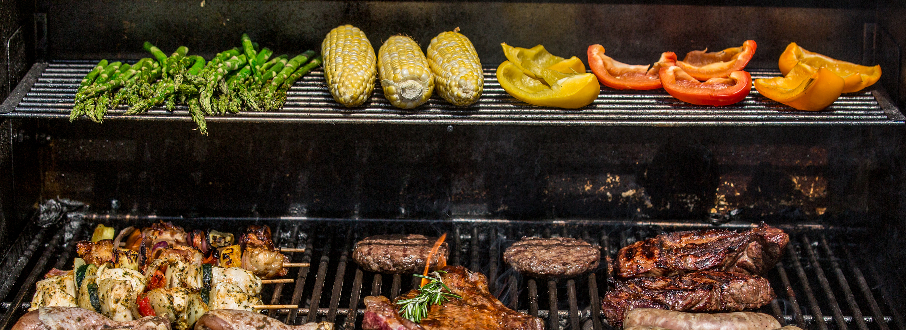 Assorted vegetables and meats on a grill with branding text.