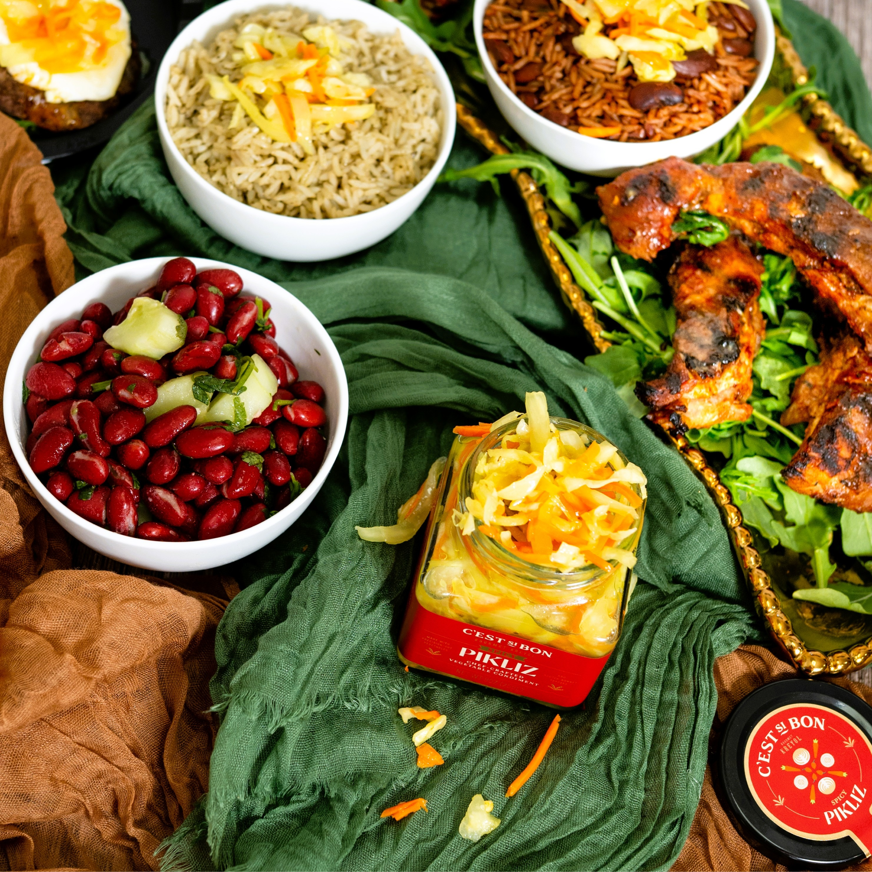 Assorted food items including beans, rice, and a jar of pickles on a green cloth.