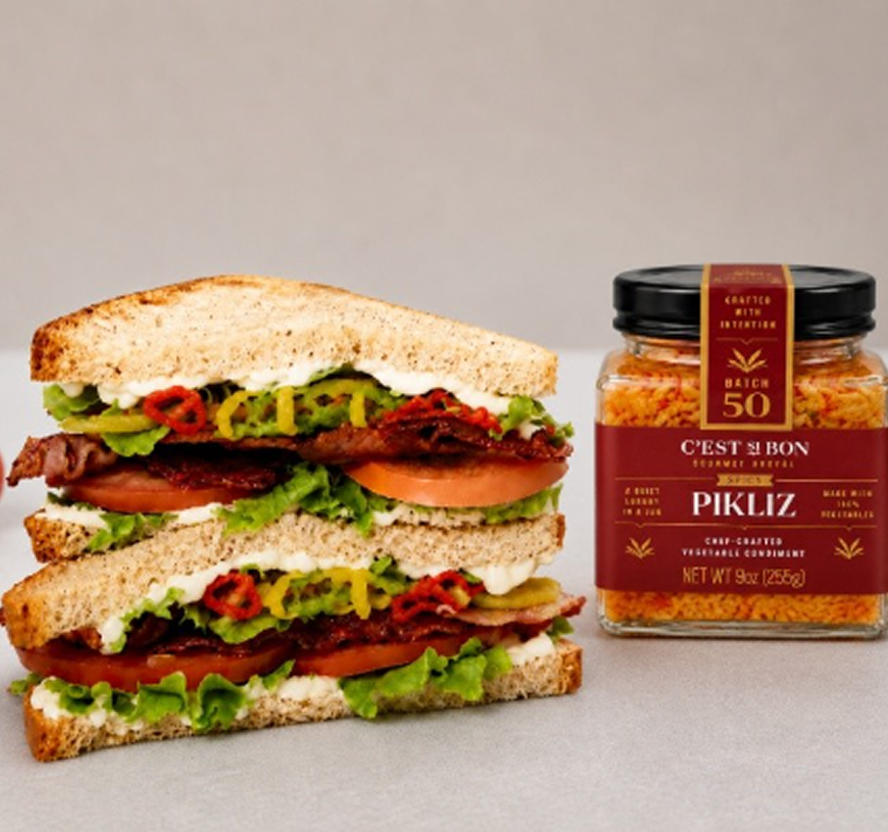 Blt sandwich and jar of Pikliz on a neutral background