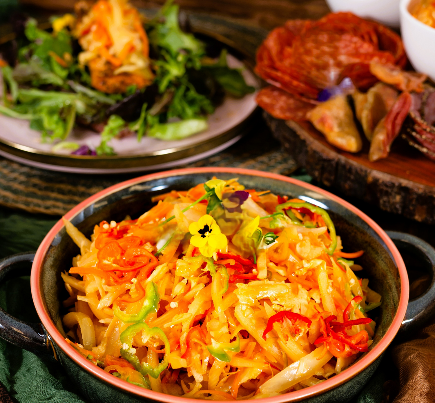 Colorful salad with shredded carrots and other vegetables in a bowl, with additional food items in the background.