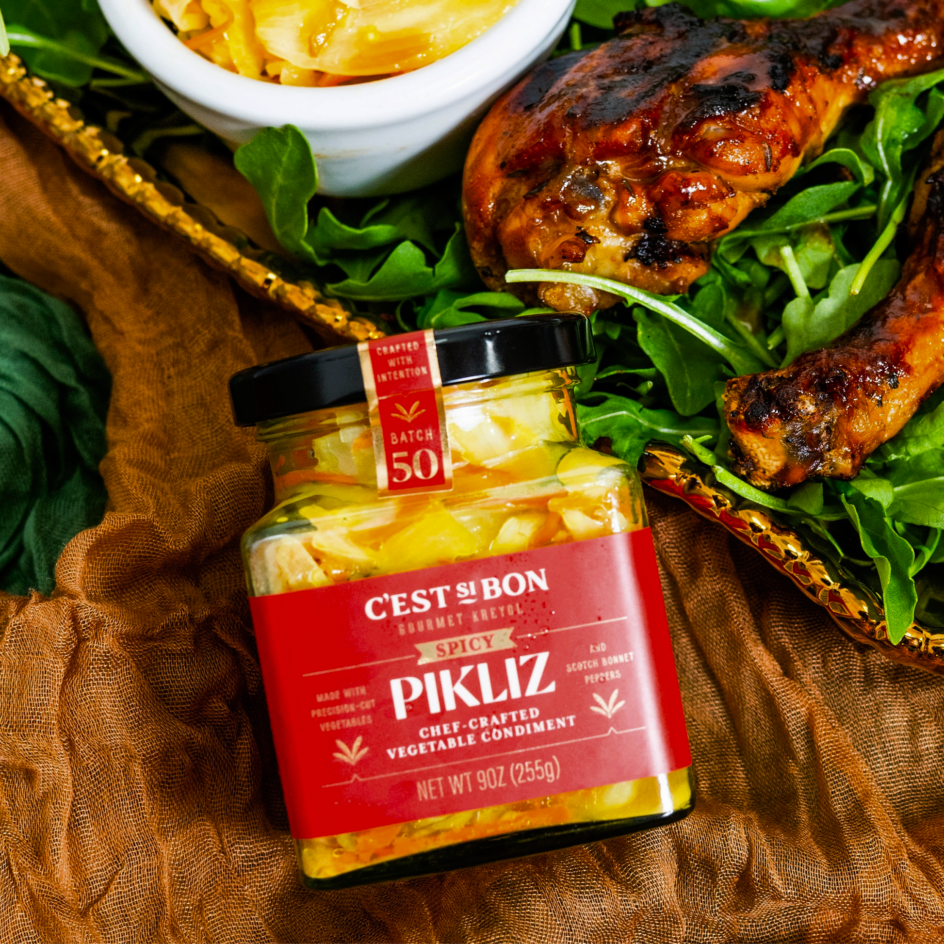 Jar of Pikliz with a salad and grilled chicken on a brown fabric background