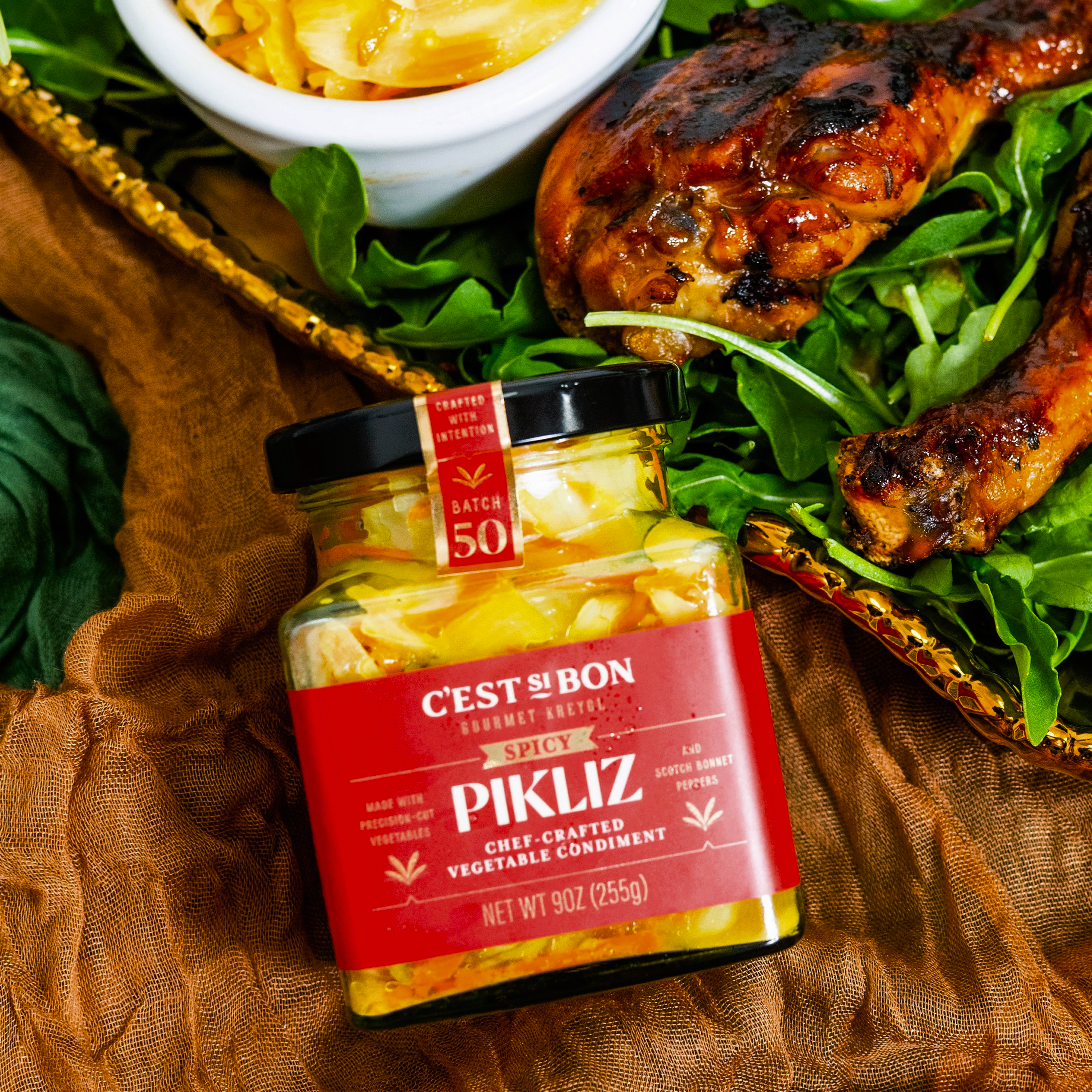 Jar of Pikliz with a salad and grilled chicken on a brown fabric background